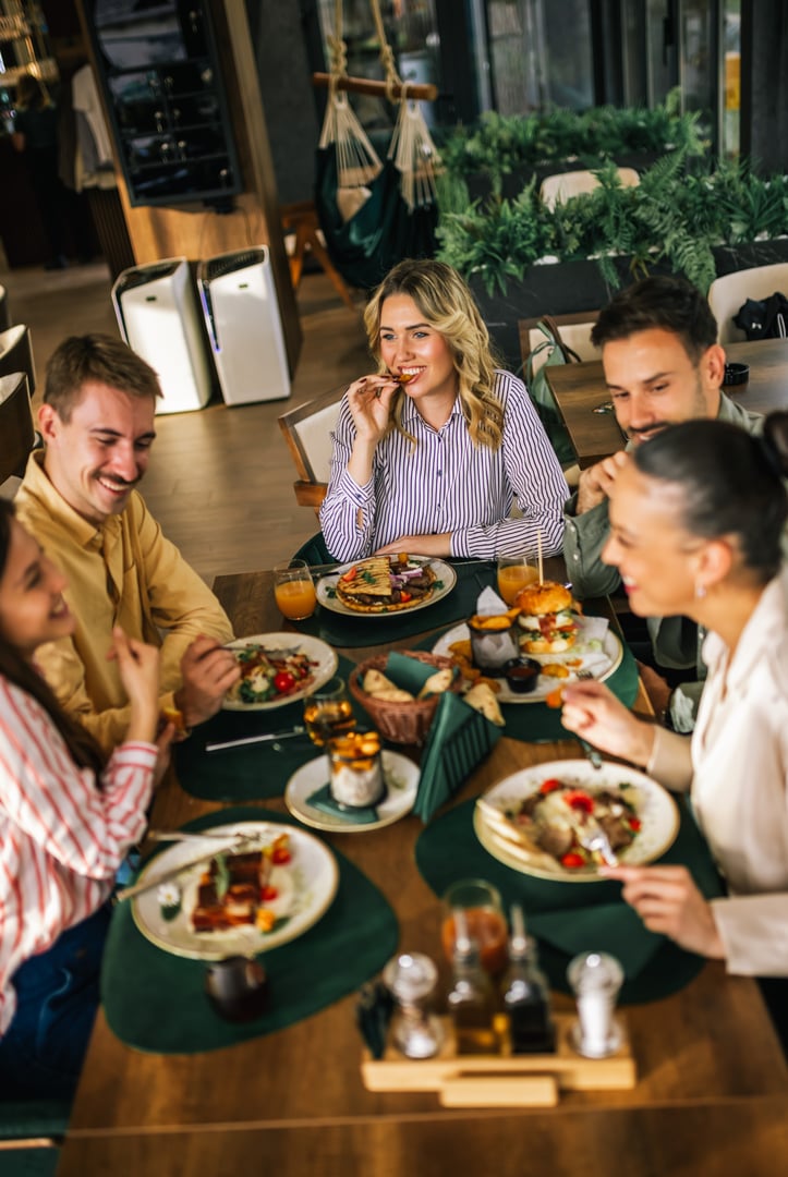 Group of happy friends eating lunch together in a restaurant. They eat delicious salads and hamburgers.