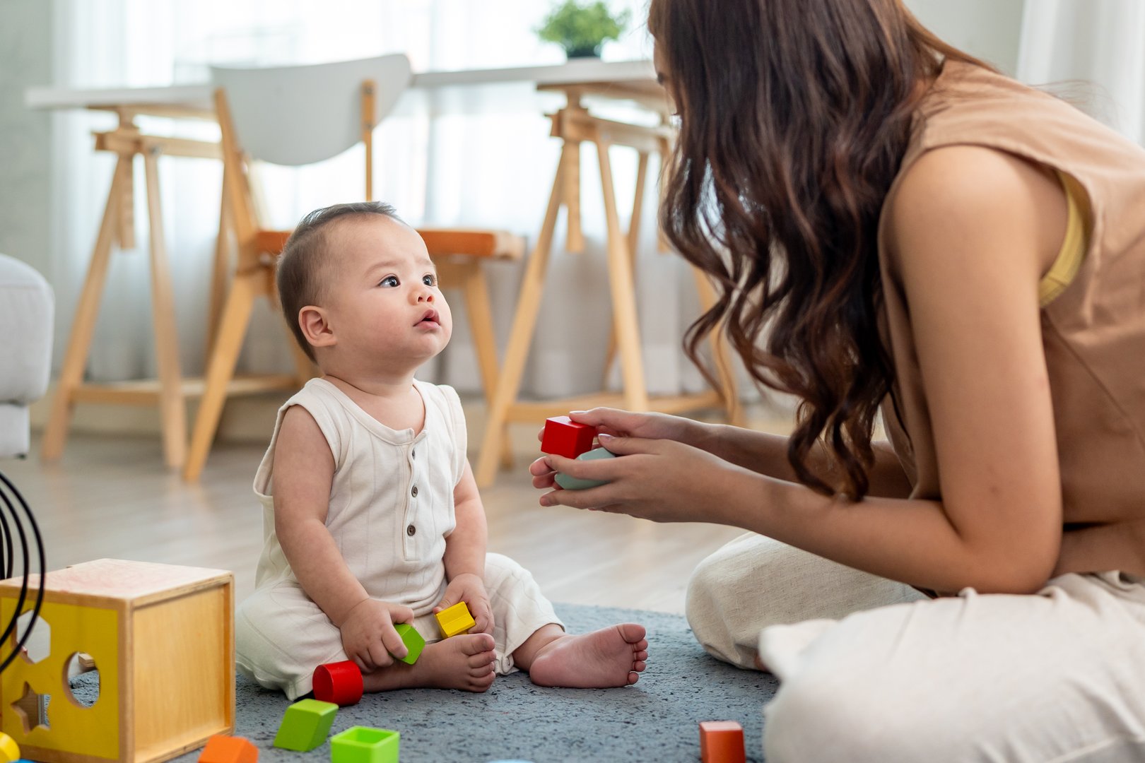 A cheerful baby playing with colorful toys with loving mother in house. Little adorable cute baby boy toddler having fun, enjoy playing on soft carpet with mom in a cozy living room at home.