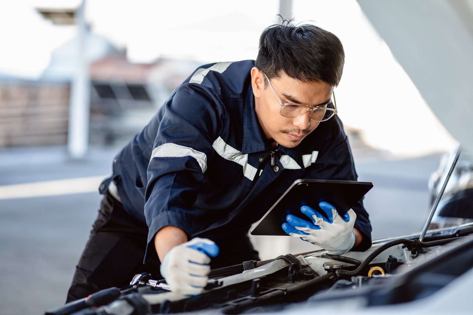 Auto mechanic repairman using a digital tablet to check the condition of engine room in the garage before changing spare parts, checking the mileage of the car, maintaining service automobile car