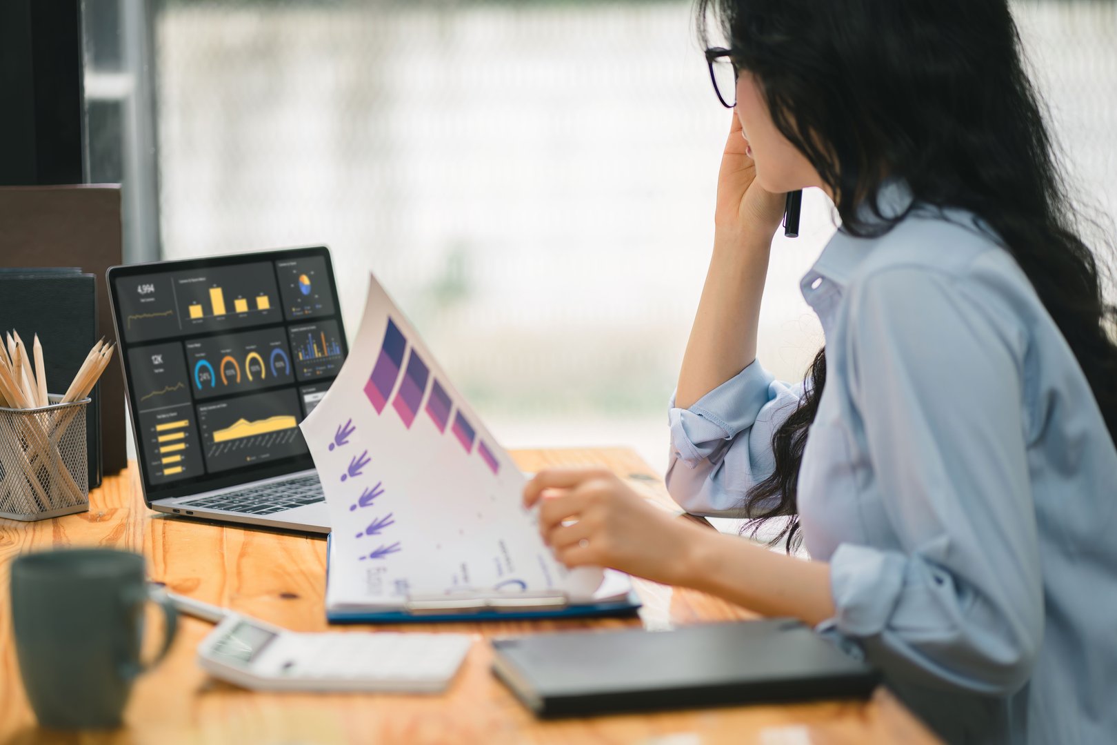Businesswoman accountant using a calculator, graphs, and charts to analyze market data, balance sheets,accounts,and net profits in order to plan new sales strategies