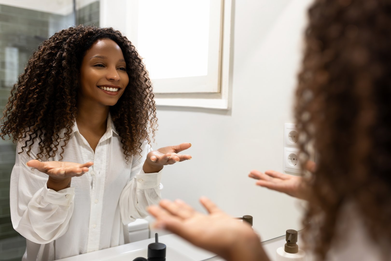Black woman motivates herself looking at her reflection in bathroom mirror. Female empowers herself, building confidence, giving pep talk before important event.Confidence and self-belief concepts.
