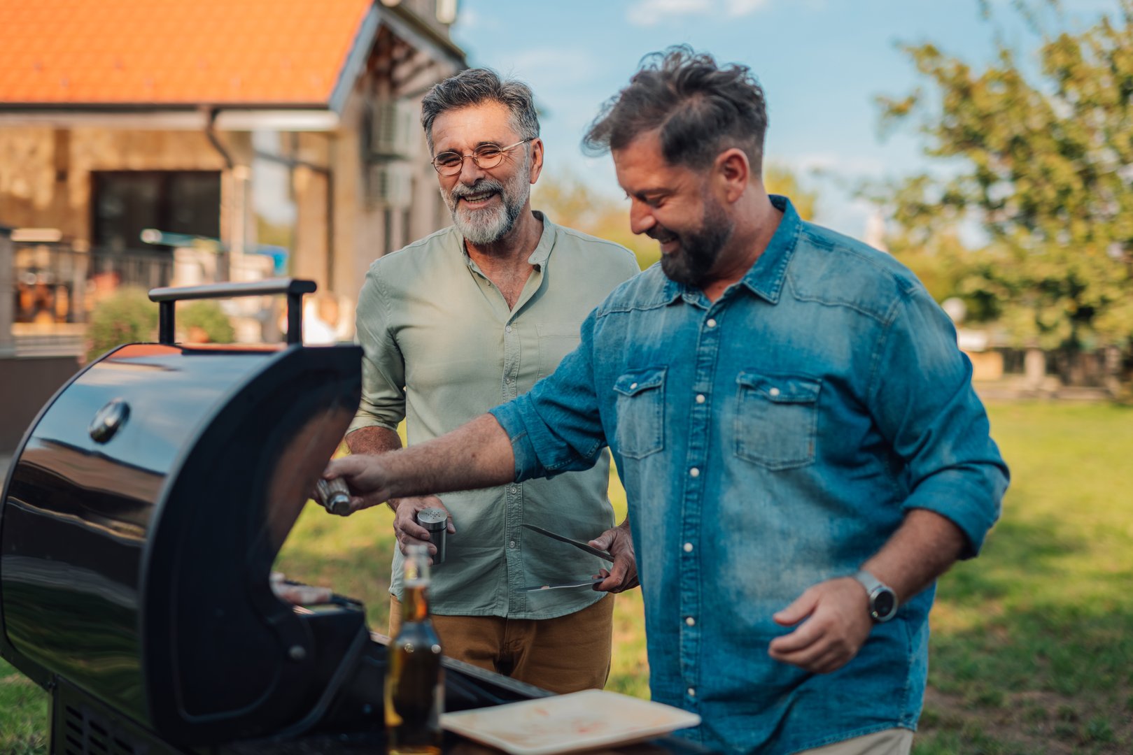 Two men are grilling food in their backyard, enjoying the summer weather