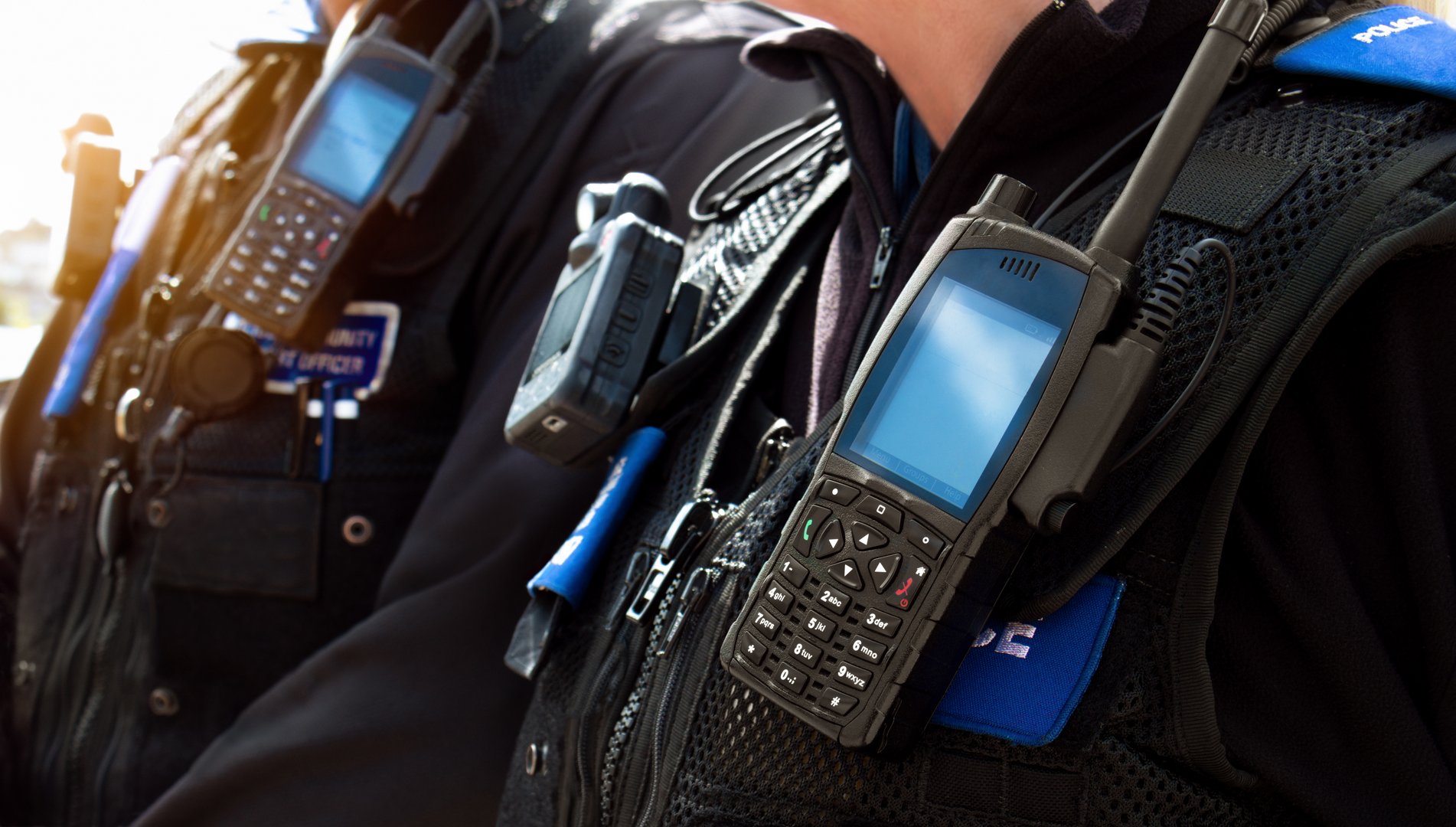 Close-up of station police officers stab proof vest uniform equipped with radio worn by a couple of department cops at the scene of an incident. Officers investigate crime, enforce the law and protect the public.