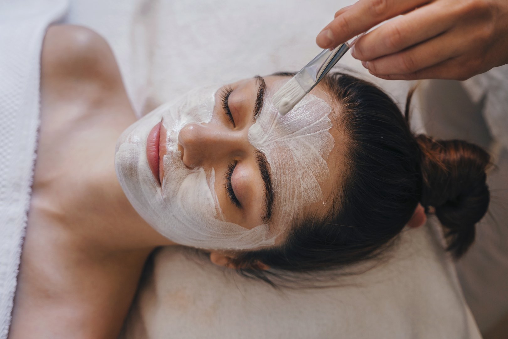 Woman getting facial nourishing mask by beautician at spa salon