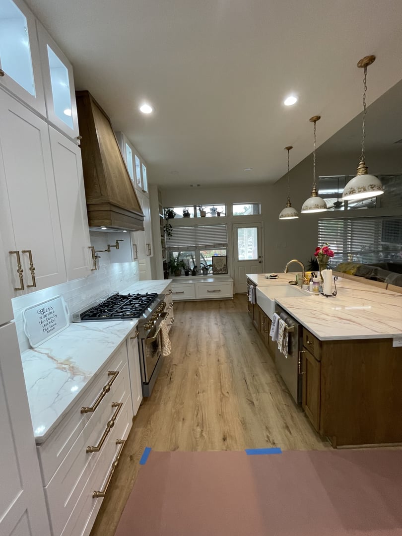 Modern kitchen with white cabinets, marble countertops, wooden flooring, and pendant lights above an island with a sink.