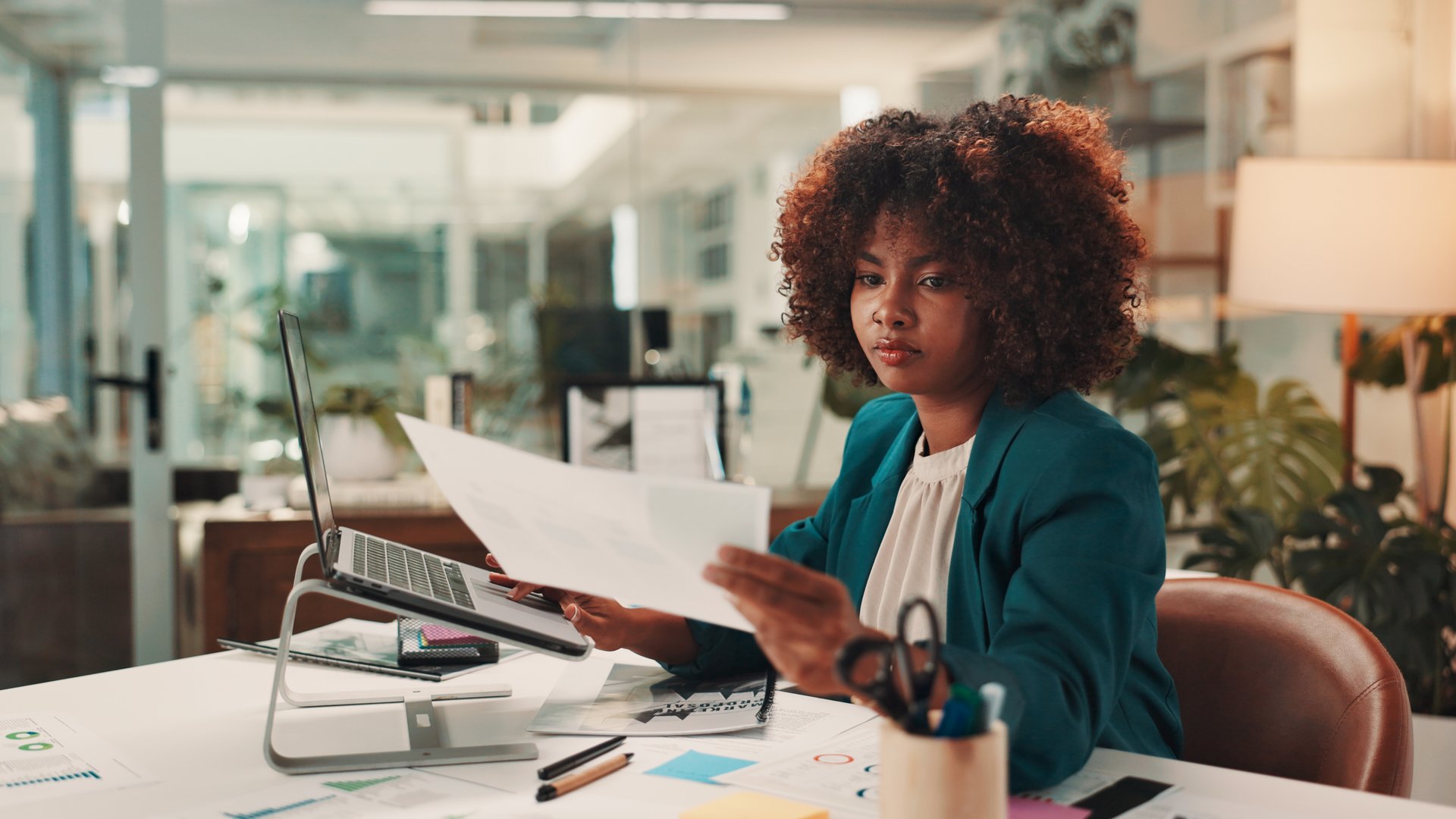 Business woman, reading and documents with laptop for web design, statistics or company report at office. Female person, creative designer or planner with paperwork, ideas or schedule for project