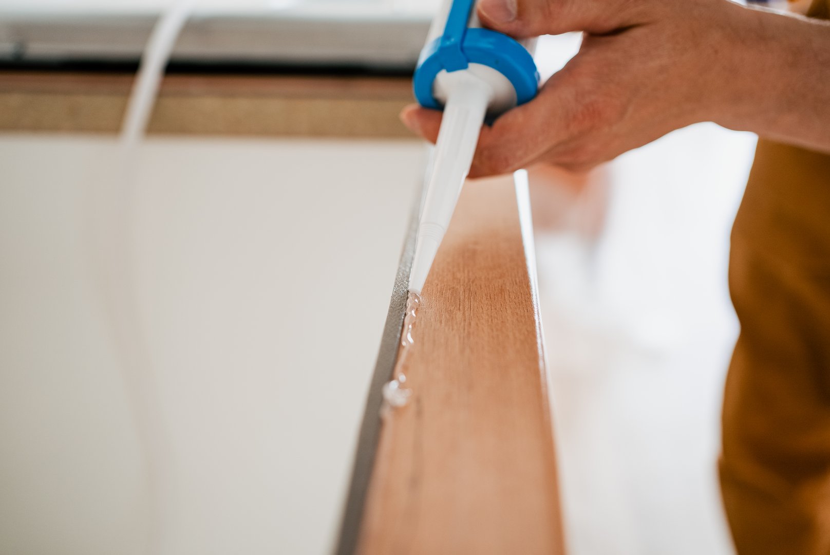 Construction worker applying silicone sealant on a wooden plank using a caulking gun, ensuring airtight and waterproof seal during renovation or installation work