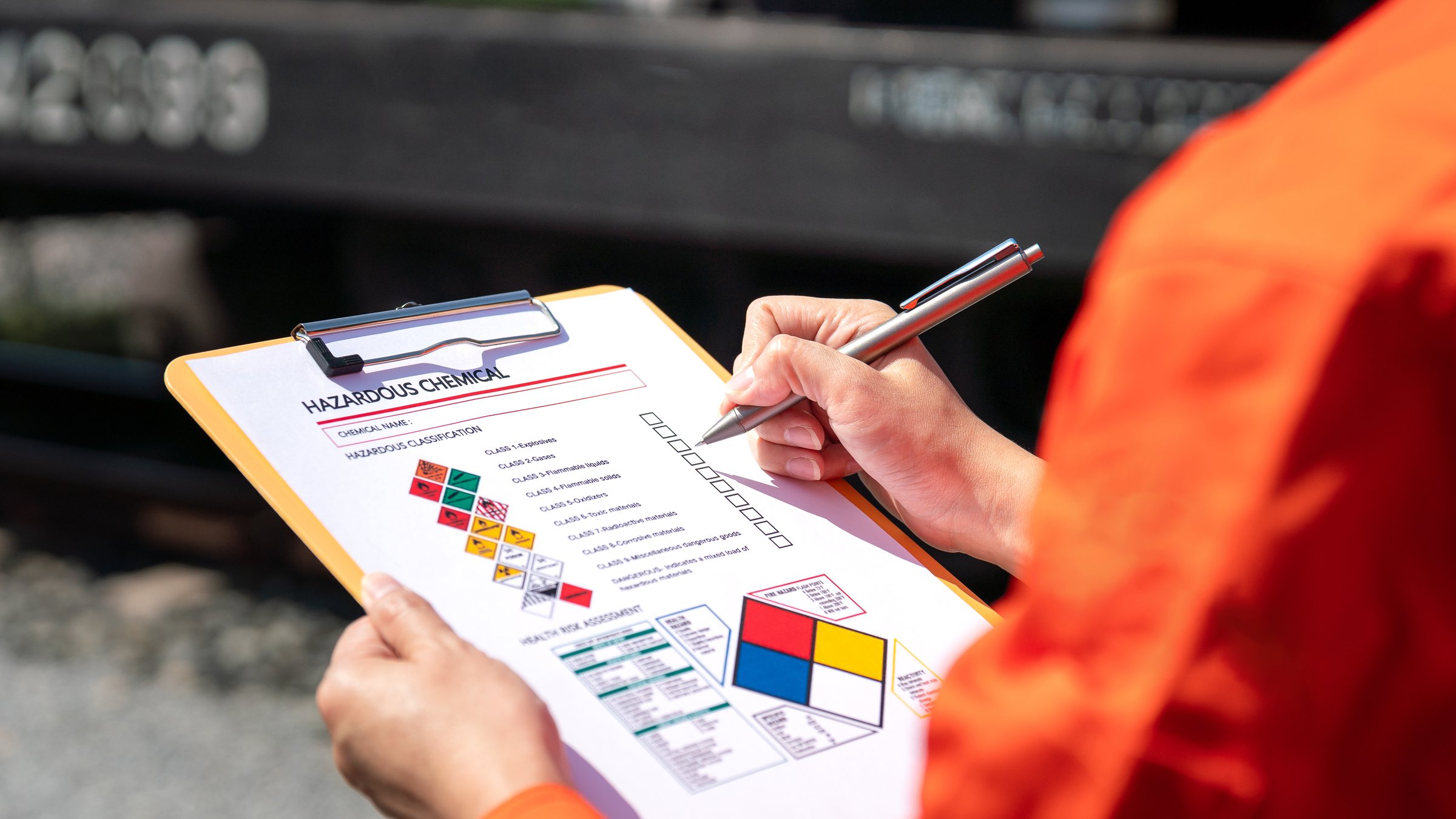 Action of an engineer is checking on chemical hazardous material checklist form with background of train freight tanker for crude oil or chemical cargo. Industrial safety working scene.