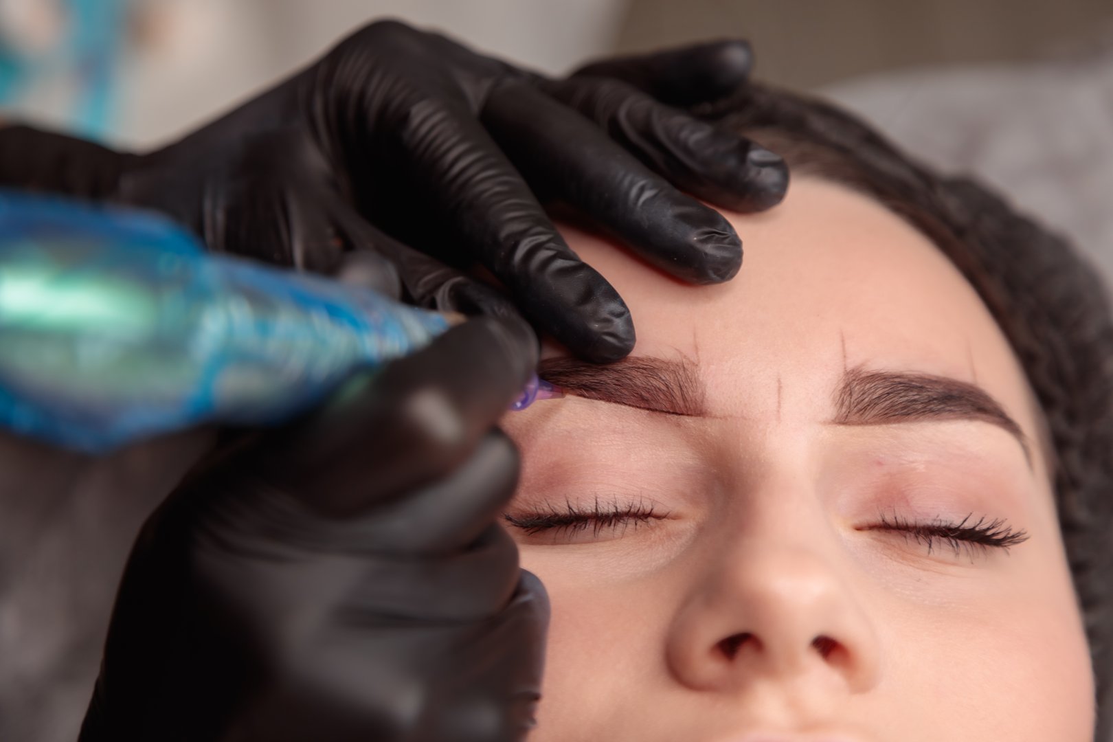 Cosmetologist making permanent eyebrow makeup using tattoo machine in beauty salon