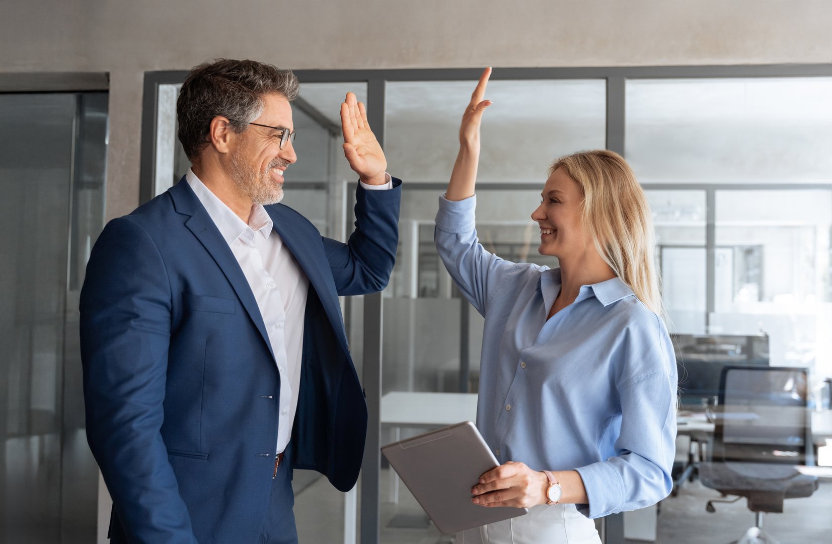 Happy smiling successful Hispanic businessman and young European professional business woman celebrating achieving superior performance, outcomes in work giving high five standing in office workspace.