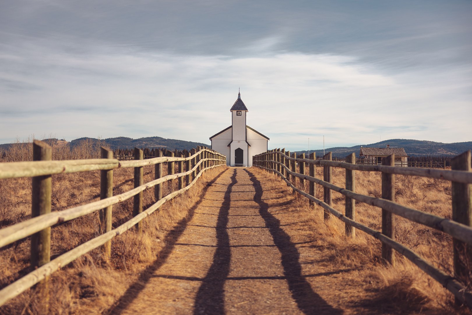 A picturesque rural church at the end of a wooden fence pathway under a partly cloudy sky.