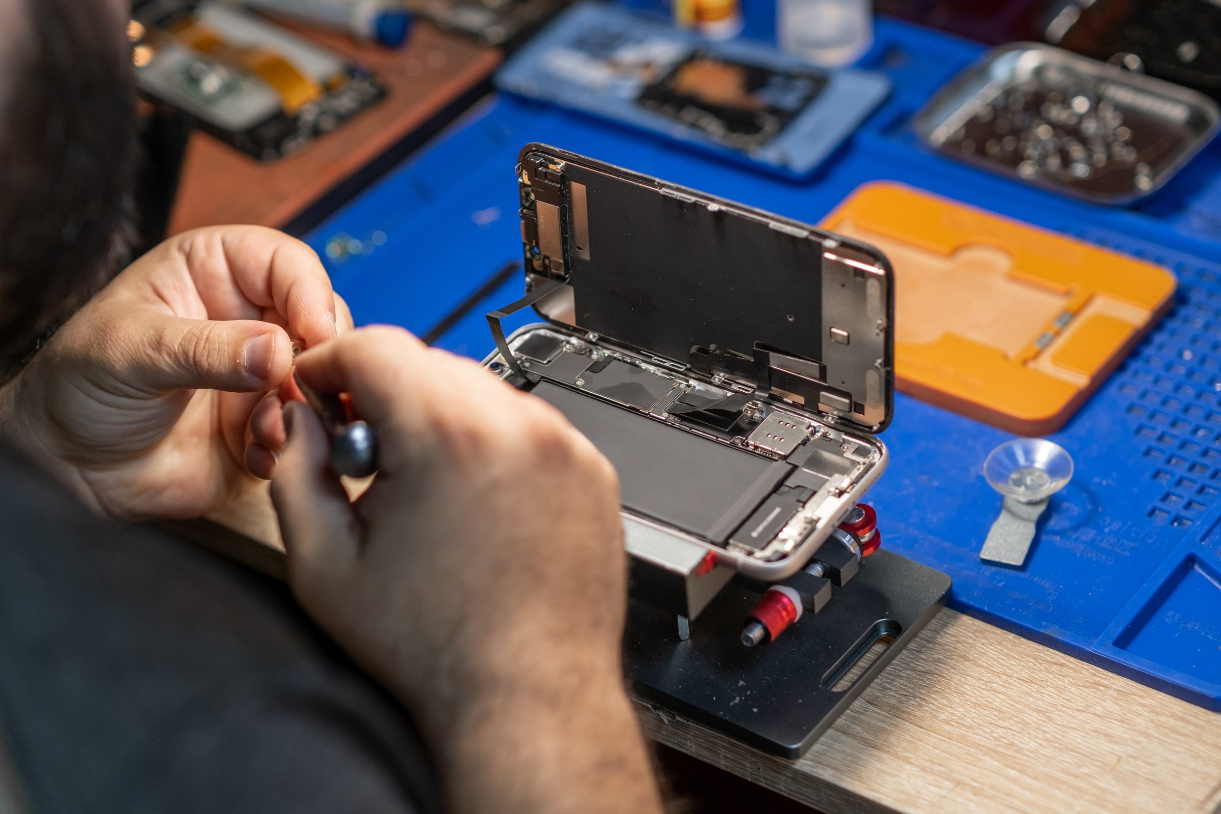 A technician focuses on replacing a smartphone battery while surrounded by tools in a repair shop.