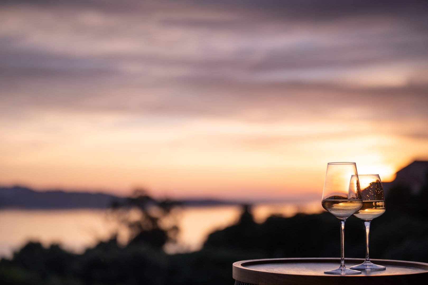 Two elegant wineglasses on a small table with the sea and sunset in the background