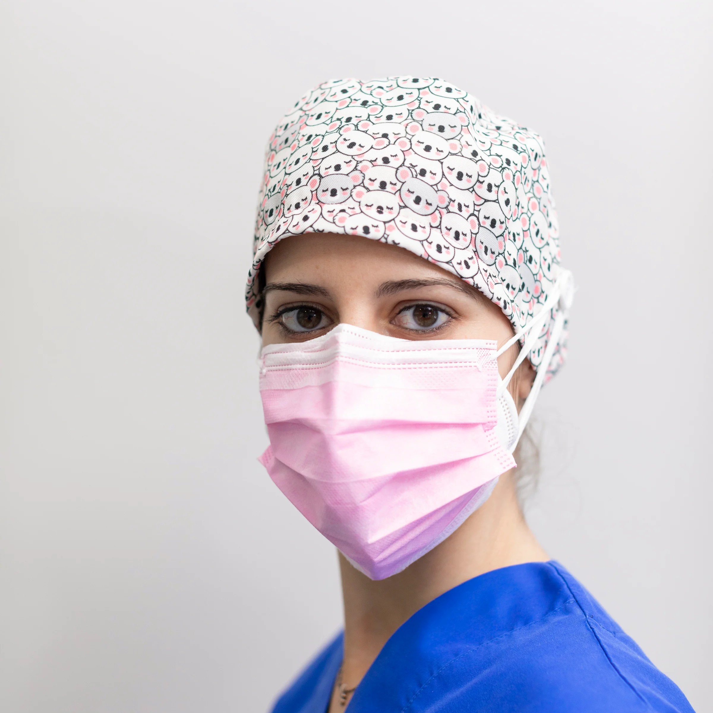 Colorful scrub cap with Disney characters in Santa hats and Christmas lights, surrounded by festive lights.