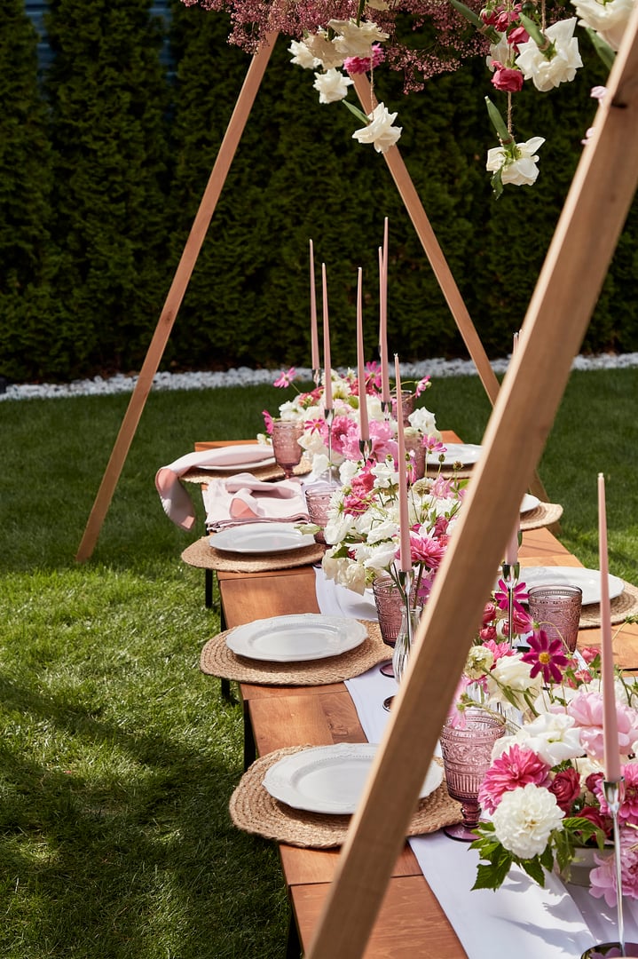 Long candles wit pink and white flowers on festive table. Visuals for event planning and design summer picnic party. Outdoor party