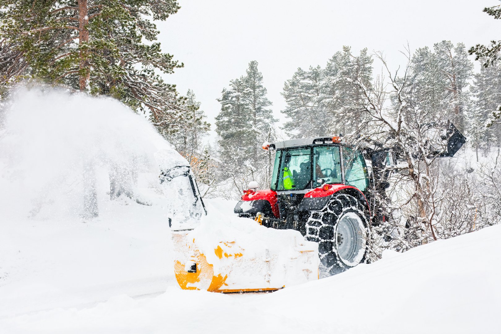 Snow removal tractor clearing heavy snow in a winter landscape, emphasizing winter property maintenance for Anchorage neighborhoods.