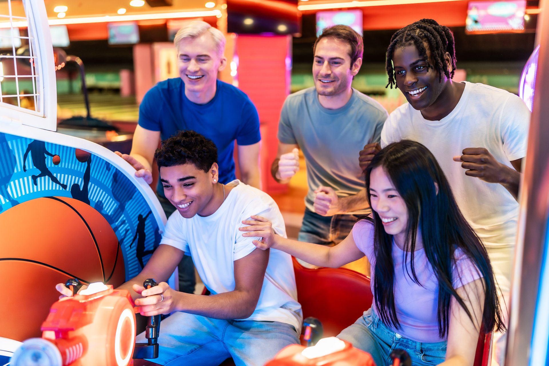 Group of cheerful multiethnic friends enjoying a fun-filled weekend at the arcade, playing basketball video game