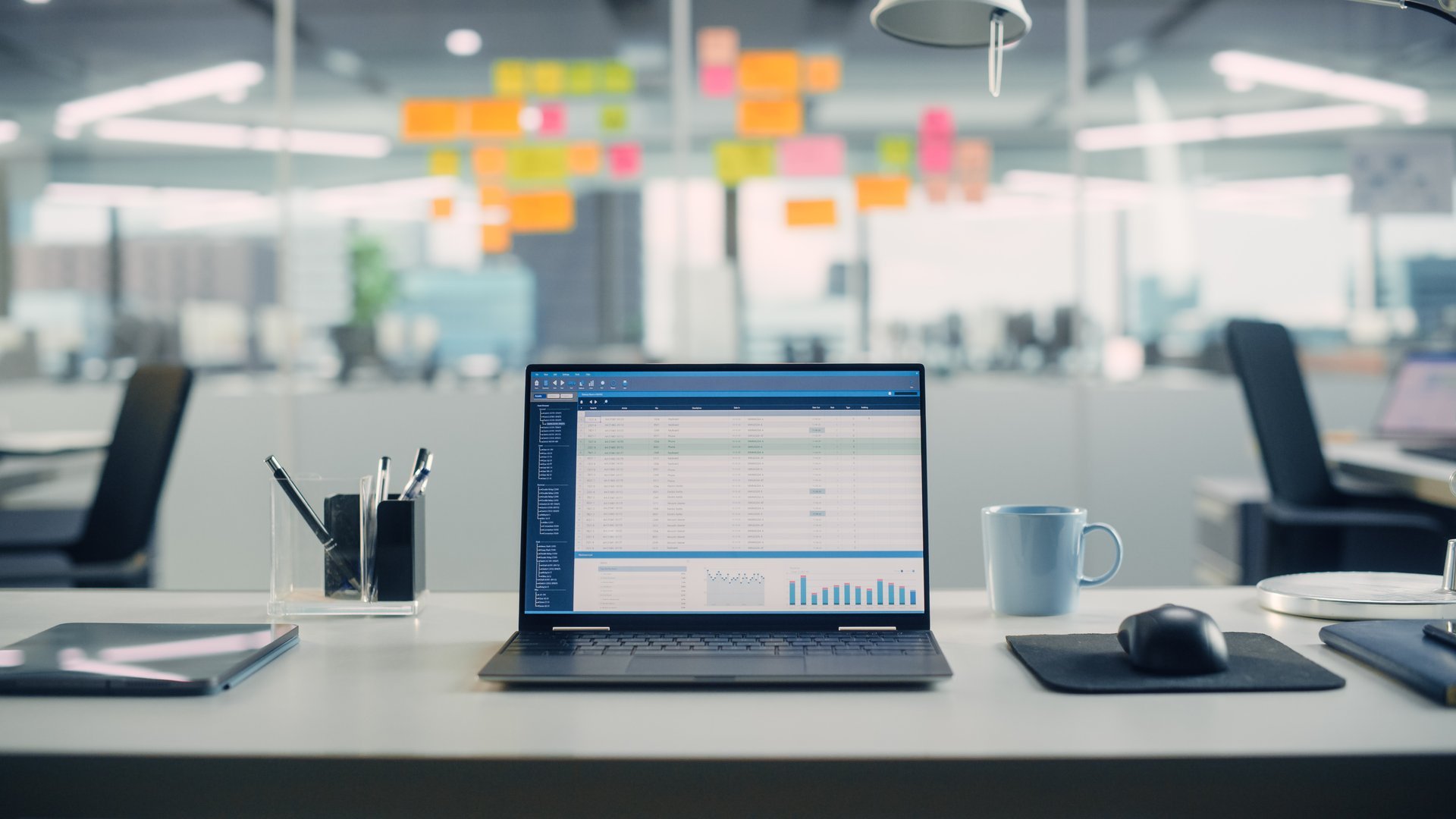 Laptop Computer with Financial Analytical Spreadsheet Application Standing on the Desk in the Modern Creative Office. In the Background Glass Wall with Colorful Planning Notes.