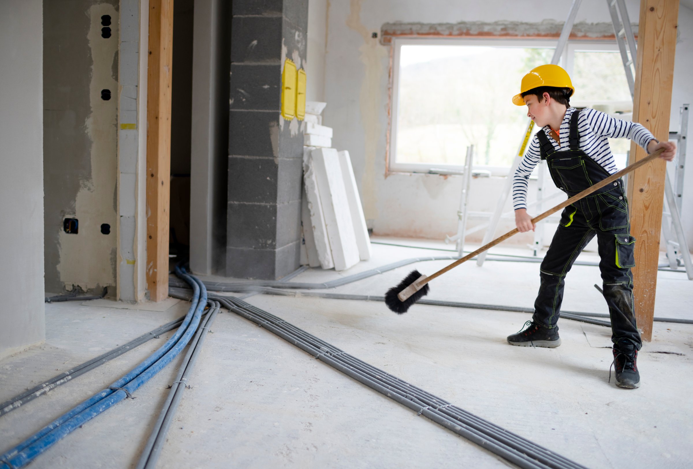 Ragazzo con casco giallo che posa in cantiere in una casa con scopa
