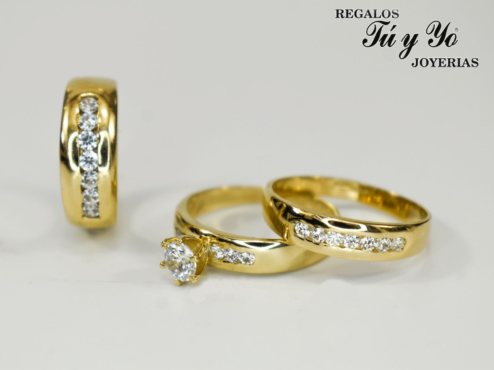 Gold rings with embedded diamonds and a solitaire diamond ring, displayed on a white surface. "Regalos Tú y Yo Joyerías" logo.