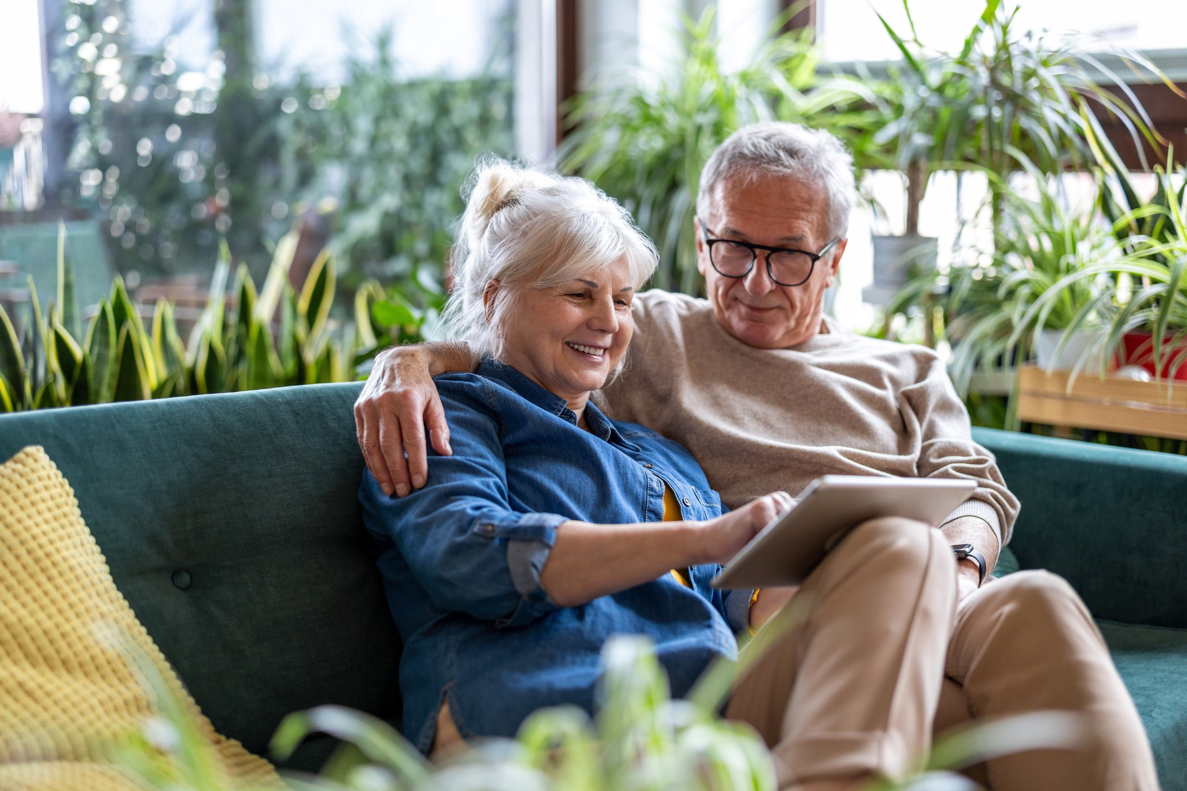 Happy senior couple using digital tablet while sitting on sofa in living room