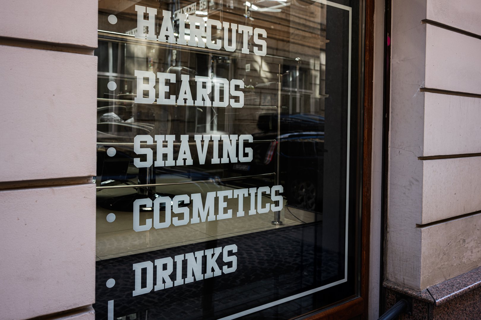 Glass window of a barber shop displaying haircut and beard services.