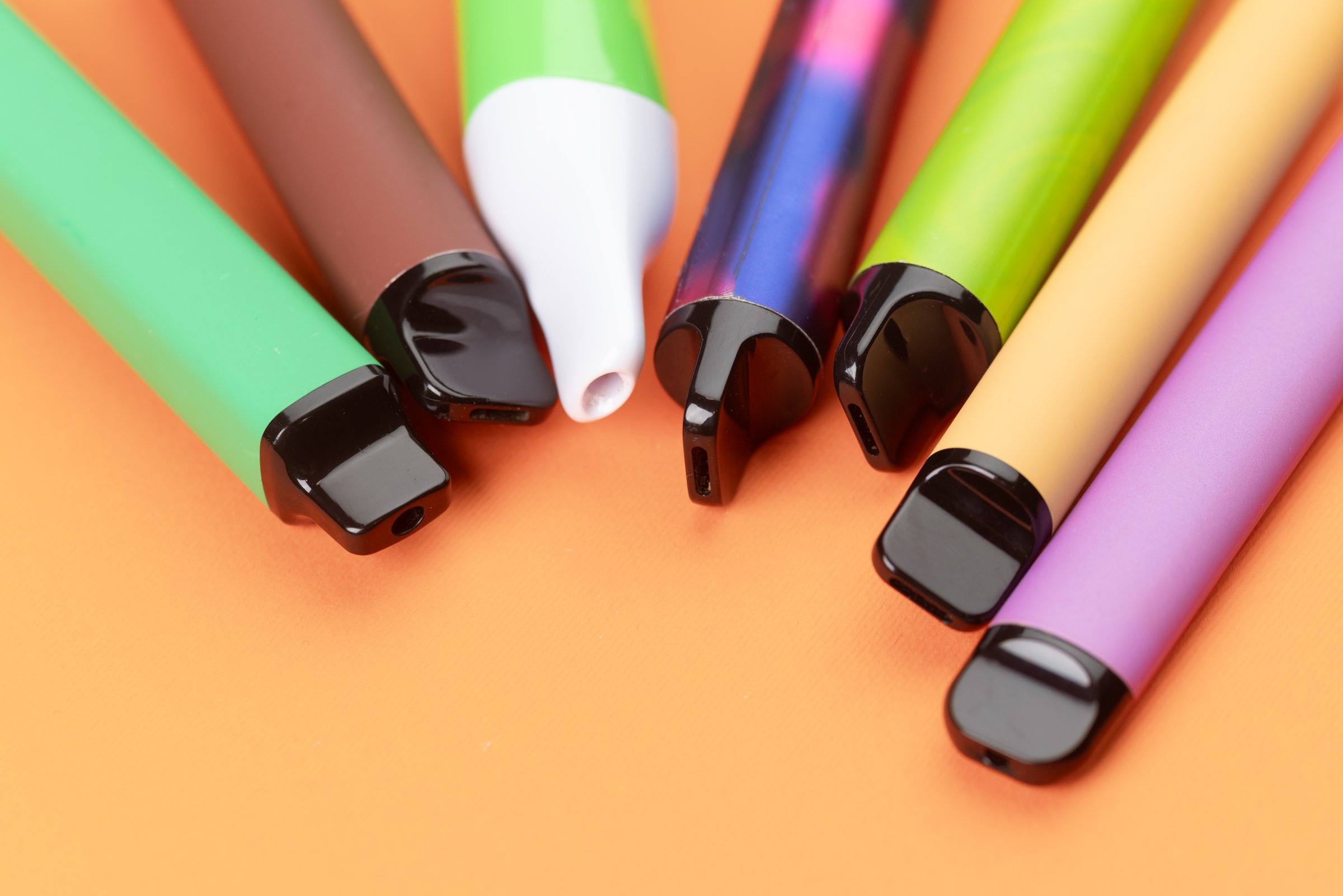 Colorful disposable vape pens on orange background, modern electronic smoking devices closeup.
