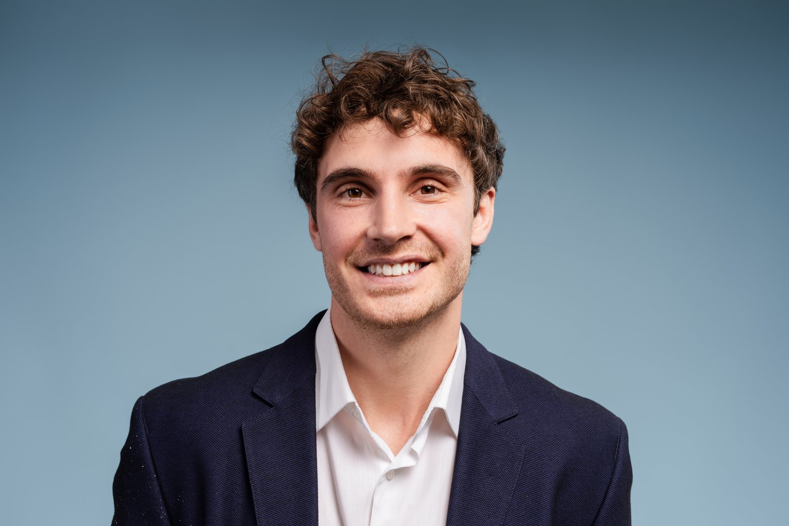 Confident, smiling businessman with curly hair on a blue background exudes success and positivity, ideal for business designs. Advertisement concept