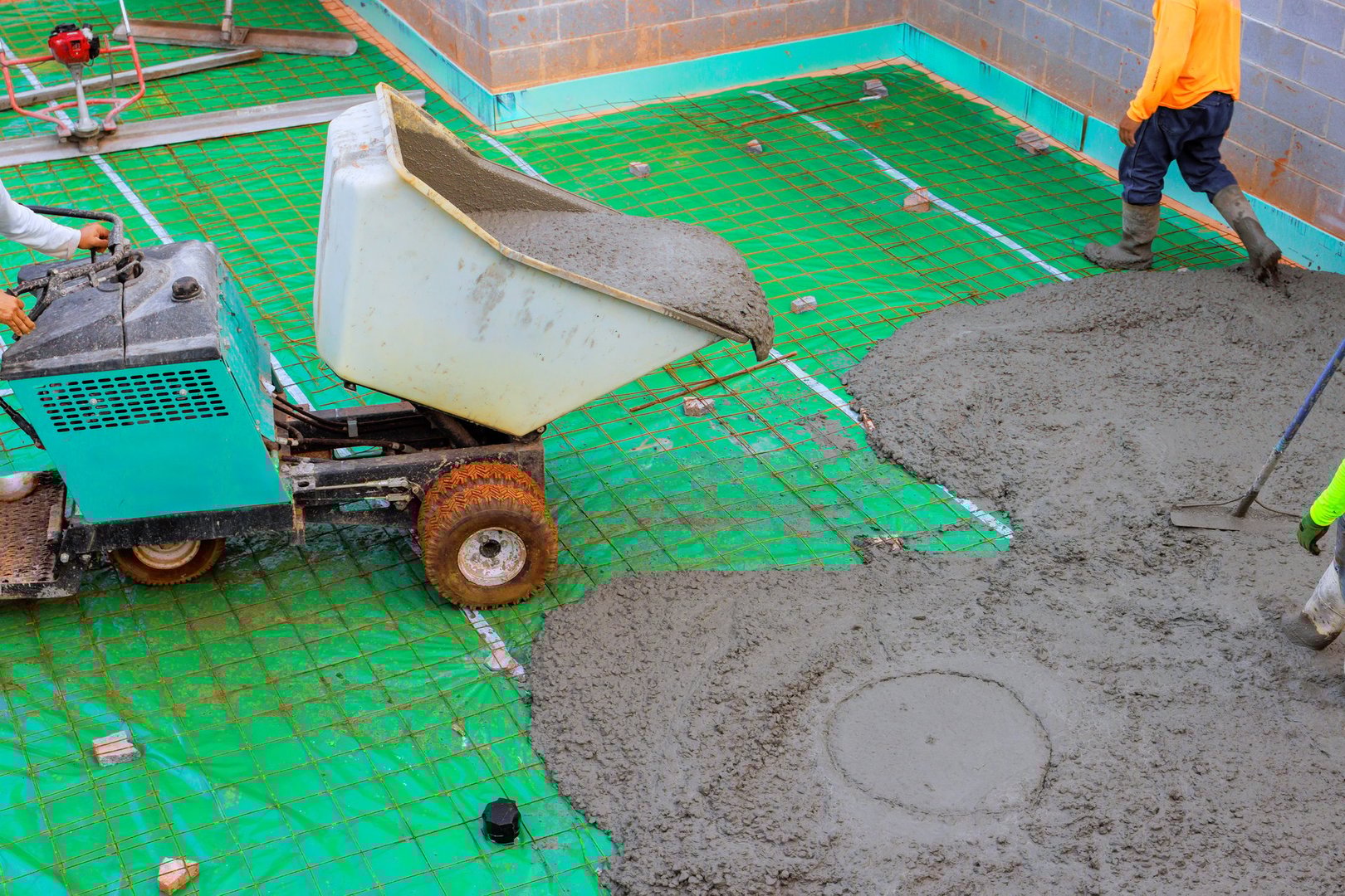Workers are pouring fresh concrete on base foundation wheeled concrete wheelbarrow usage at construction site.