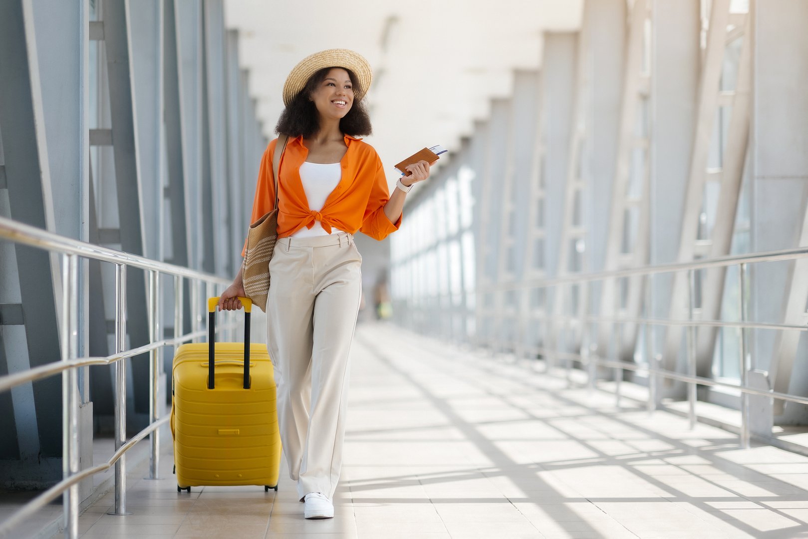 Vacation Travel. Beautiful Young Black Woman Wearing Straw Hat Walking With Suitcase In Airport Terminal, Happy Smiling African American Lady Ready For Trip, Going To Departure Gate, Copy Space
