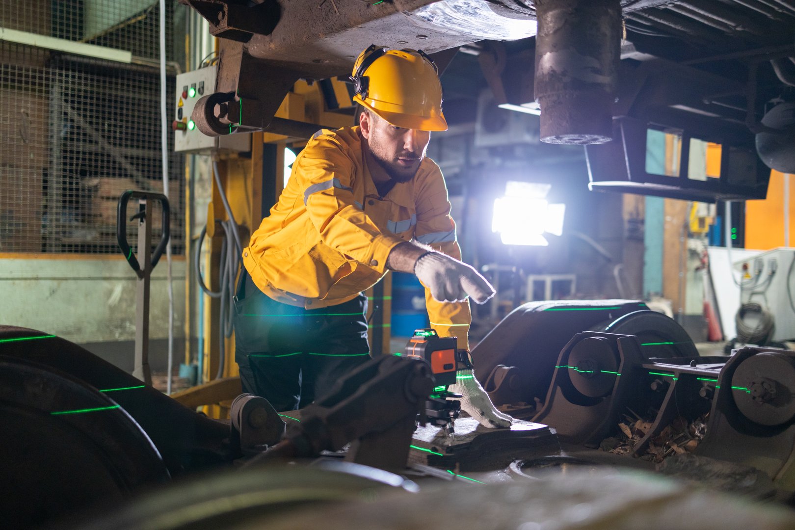 Railway technicians in reflective safety gear conducting detailed undercarriage inspections in a maintenance workshop.