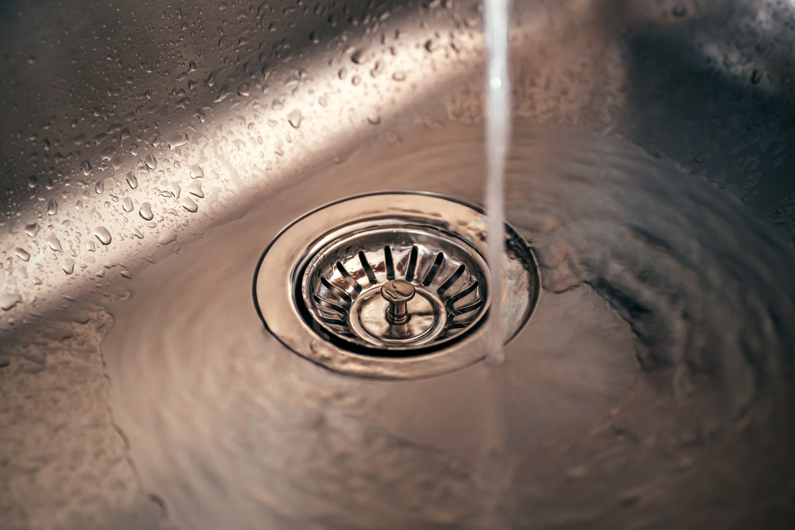 Water in new metallic kitchen sink drain, selective focus