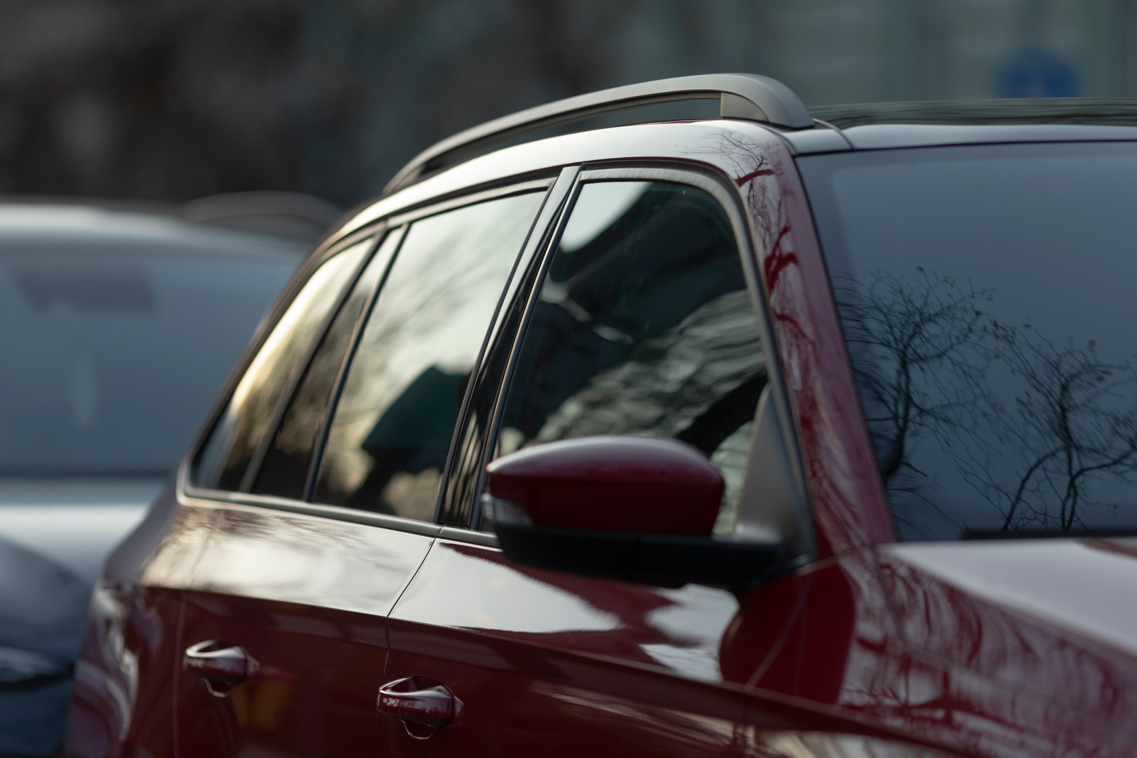 A closeup view of a bright red car, focusing on its side window and door mirror, beautifully capturing the reflections and intricate vehicle design within a bustling urban parking lot