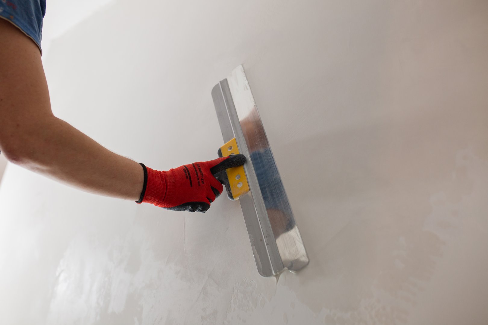 A professional finisher painter levels the walls with putty with a wide spatula