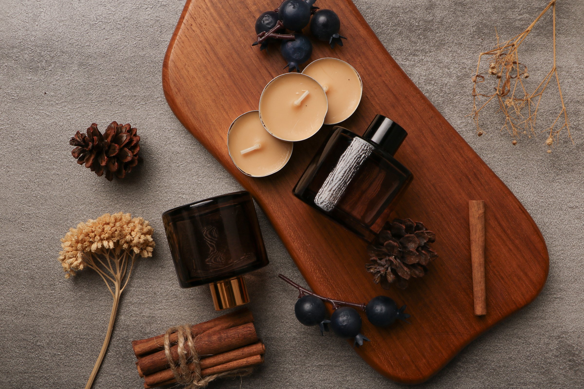 This captivating image showcases an amber glass bottle with a gold cap, perfect for storing luxurious skincare or fragrance products. The bottle is artfully arranged on a wooden tray alongside elements of nature, such as pinecones, cinnamon sticks, and dark berries. The addition of tealight candles adds a warm and inviting glow, creating a cozy, spa-like atmosphere. This setting is ideal for brands promoting natural, eco-friendly, or artisanal products, evoking a sense of relaxation and organic beauty. Perfect for ads, websites, or social media visuals in the wellness, beauty, and aromatherapy industries.