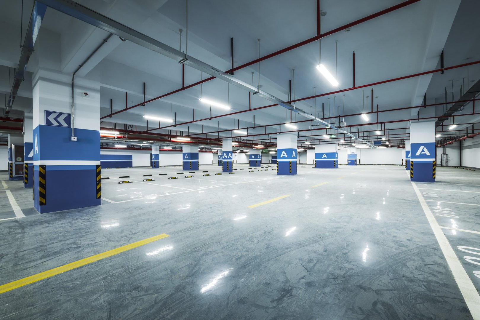Brightly illuminated empty modern underground parking garage interior features concrete floor and support pillars background.