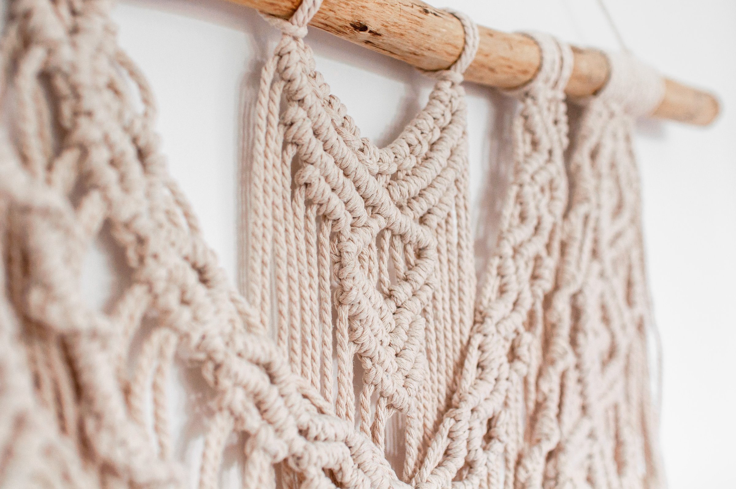 Wall decor in the style of weaving macrame handmade from beige natural threads on a white background