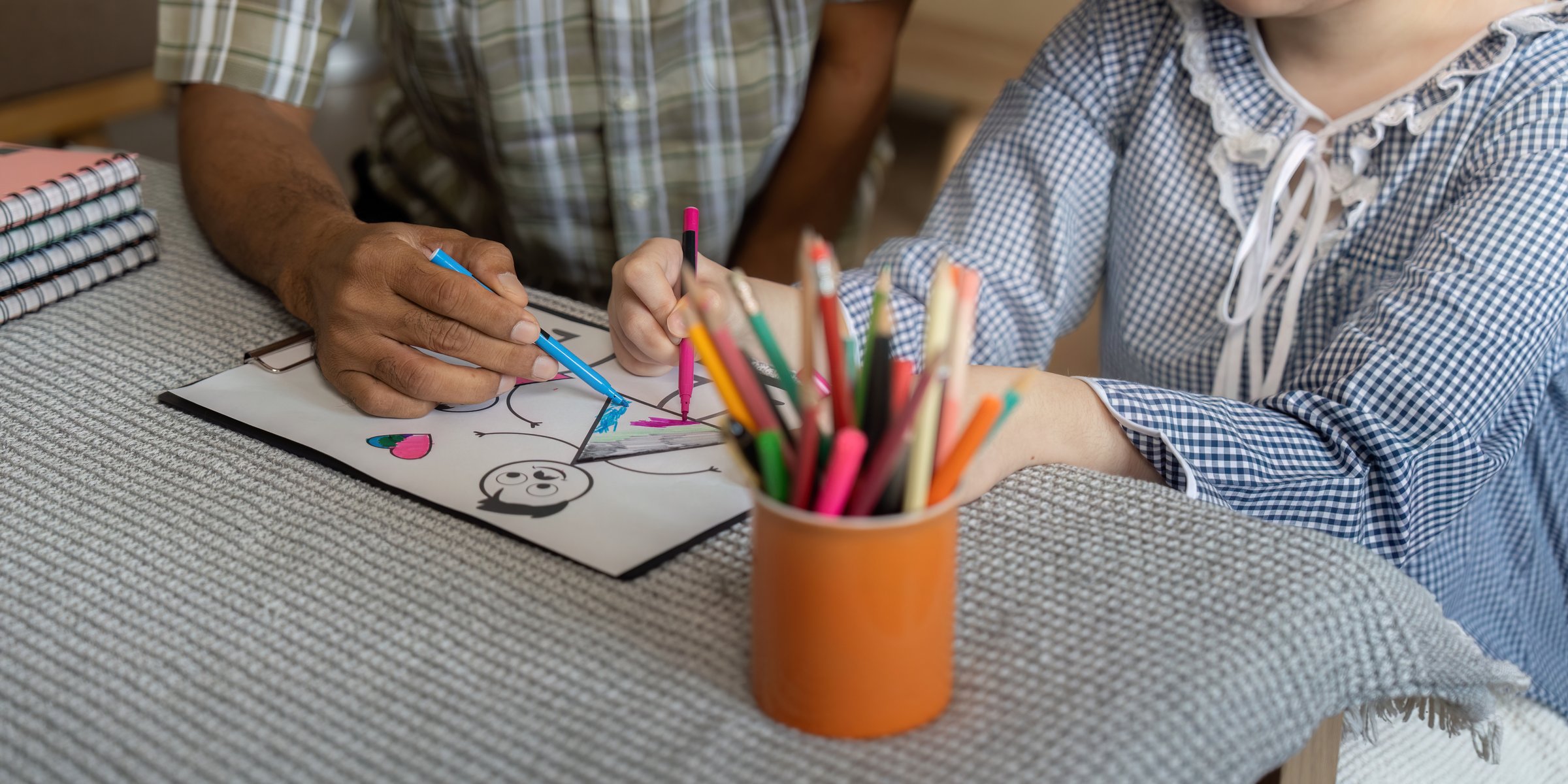 In a cozy setting, a caregiver helps a teenage girl with Down syndrome as she explores her artistic skills through drawing, promoting creativity and confidence.