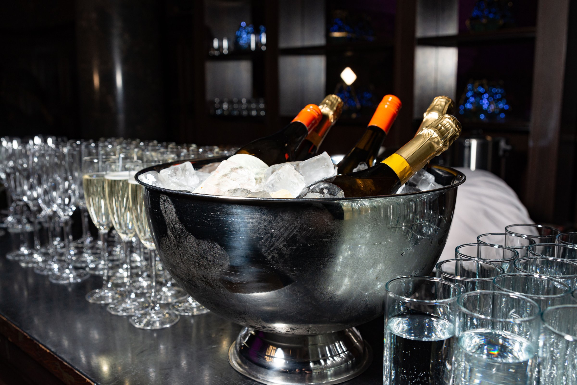 Chilled champagne bottles in a metal bowl with ice, surrounded by glasses, prepared for a festive celebration or event.