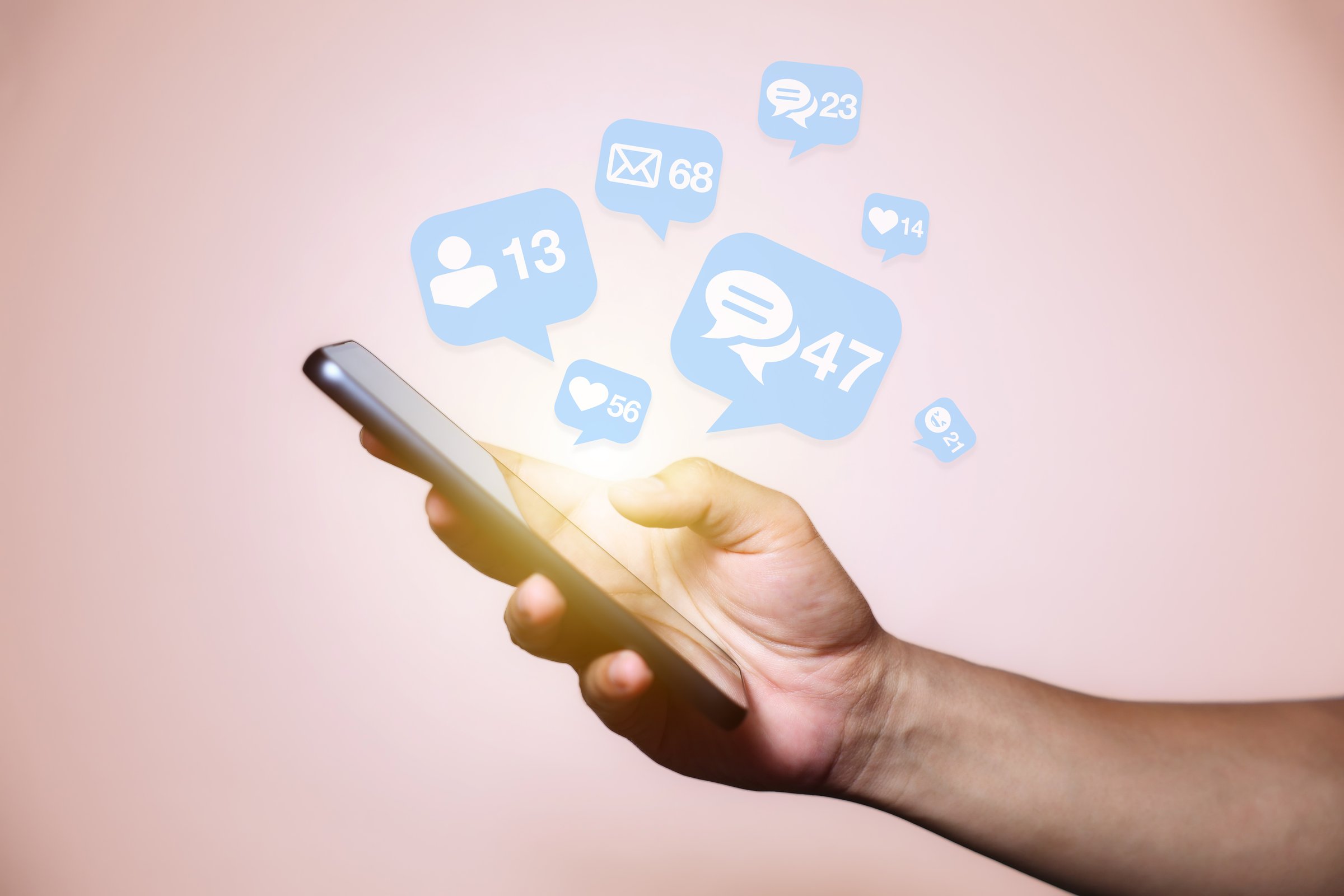 Close-up of man's hand using smartphone to play social media with emoticons or notifications popup.