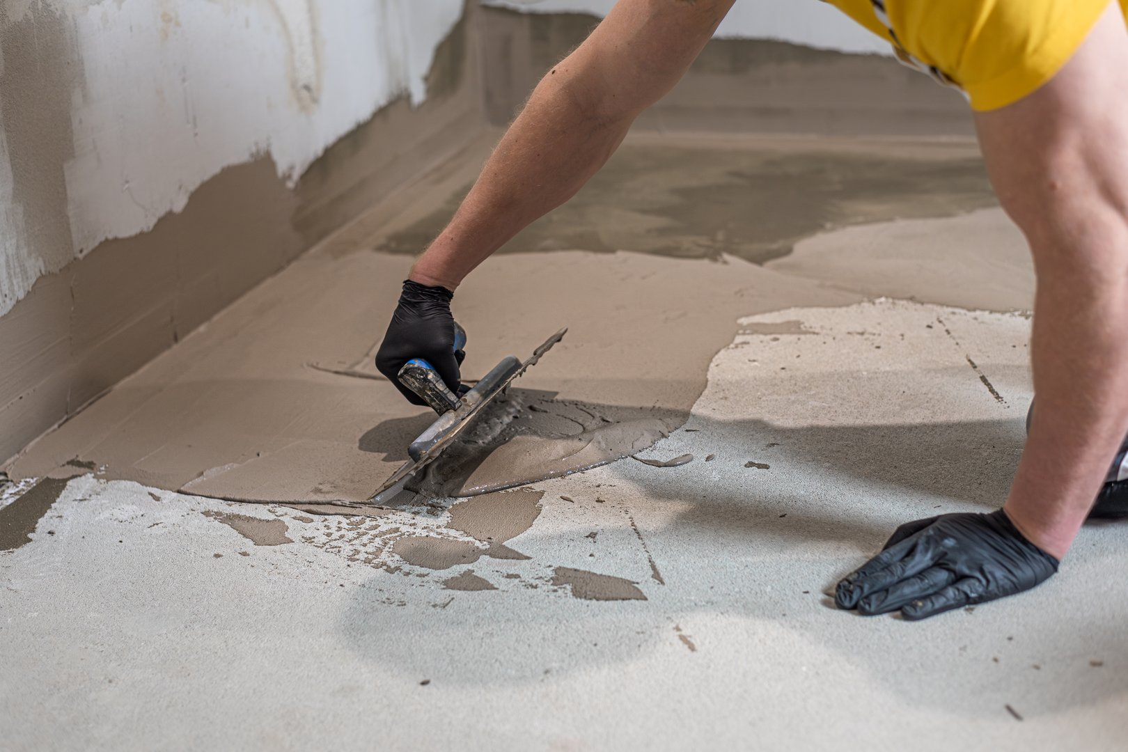 A worker's hand using a trowel for applies a  liquid membrane on the bathroom floor. Foolproof waterproofing for a tile bathroom.