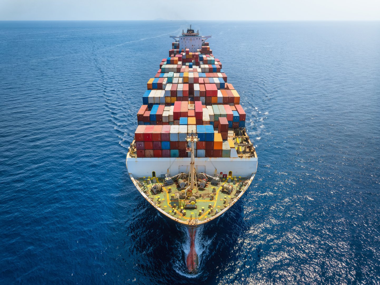 Aerial front view of a big cargo container carrier ship sailing over the ocean with speed