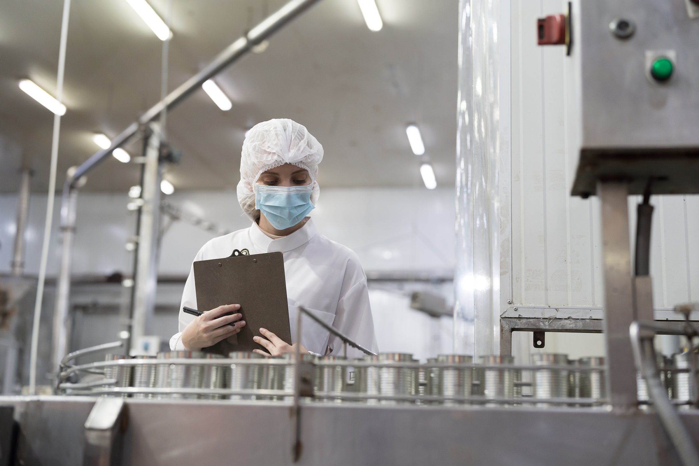 Canned fish factory, seafood manufacturing and processing. Food processing. Conveyor belt and workers. Worker in protective gear wearing hairnet inspecting quality of seafood processing conveyor belts