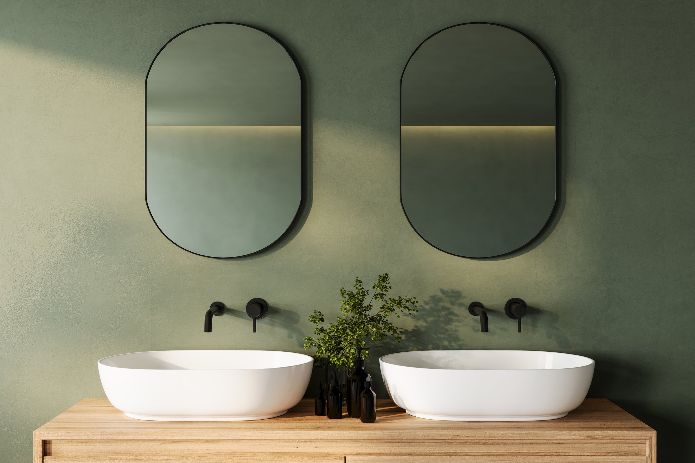 A sleek and modern bathroom vanity with dual oval mirrors, white vessel sinks, and black faucets, set against a muted green wall and wooden countertop. Enhanced with greenery for a calm, 3D Rendering