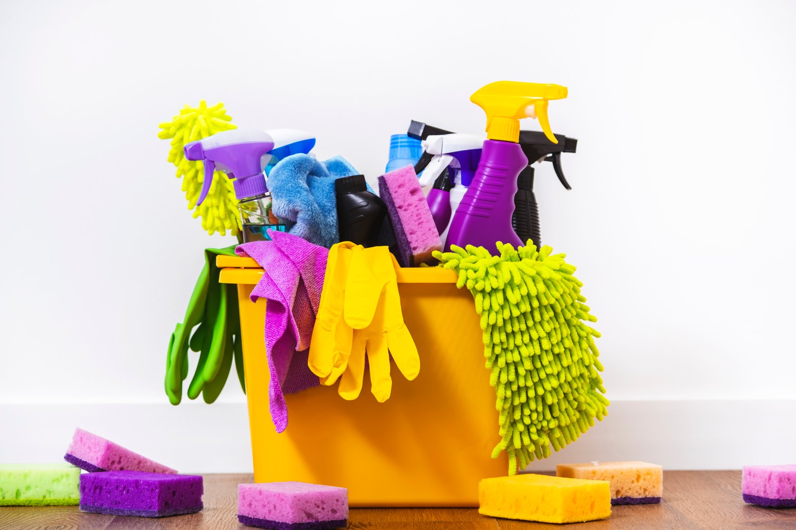 Multi-colored household chemicals, cleaning products, bottles and sprays, rags, sponges, gloves in orange bucket for washing, wiping and dusting