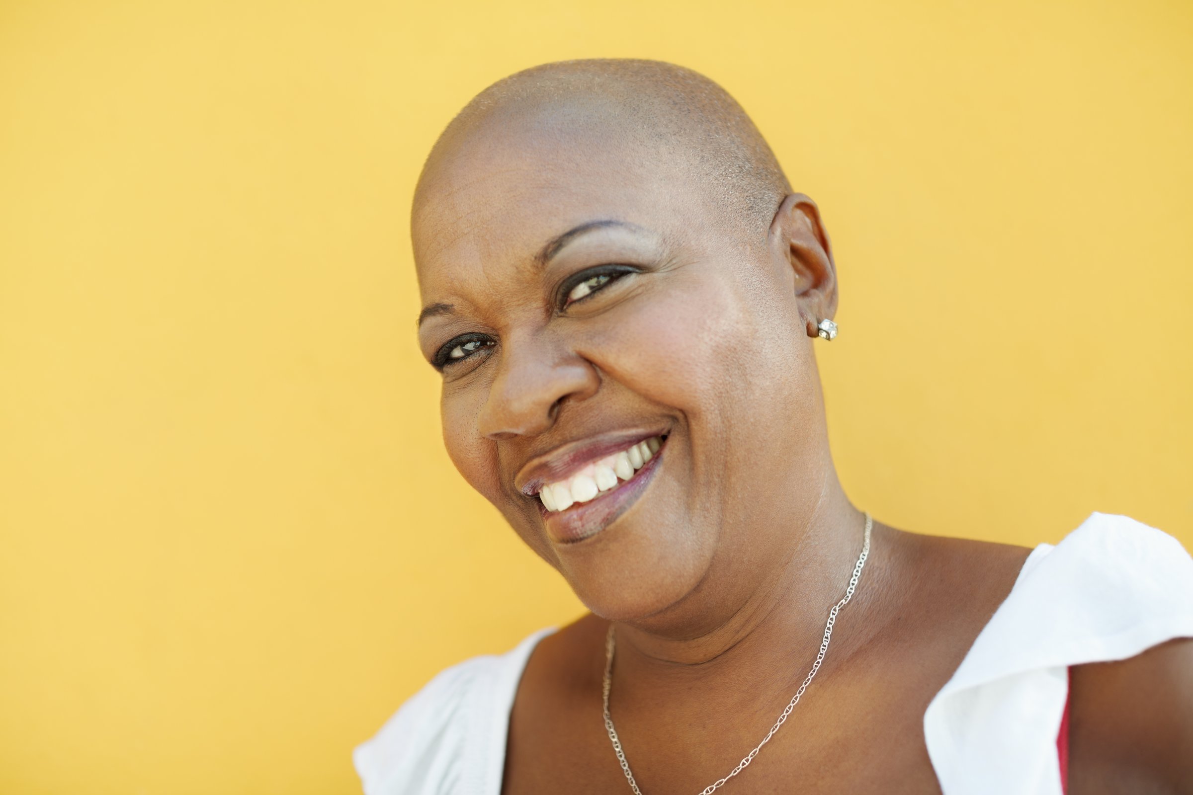 portrait of african 50 years old woman with bald head smiling at camera on yellow background. Head and shoulders, copy space
