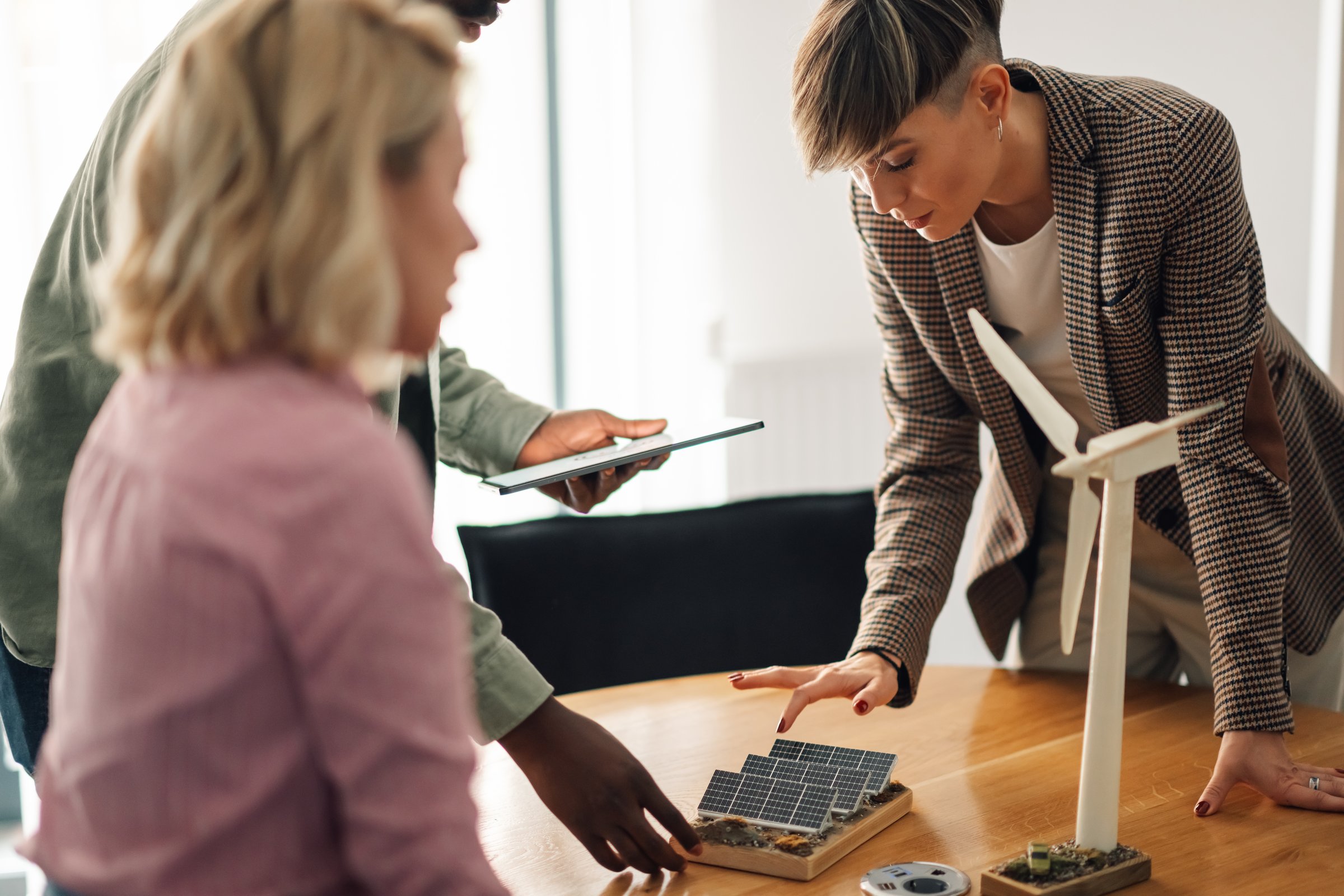 Engineers are discussing renewable energy solutions, analyzing miniature wind turbine and solar panel models during a collaborative meeting, highlighting their commitment to sustainable practices