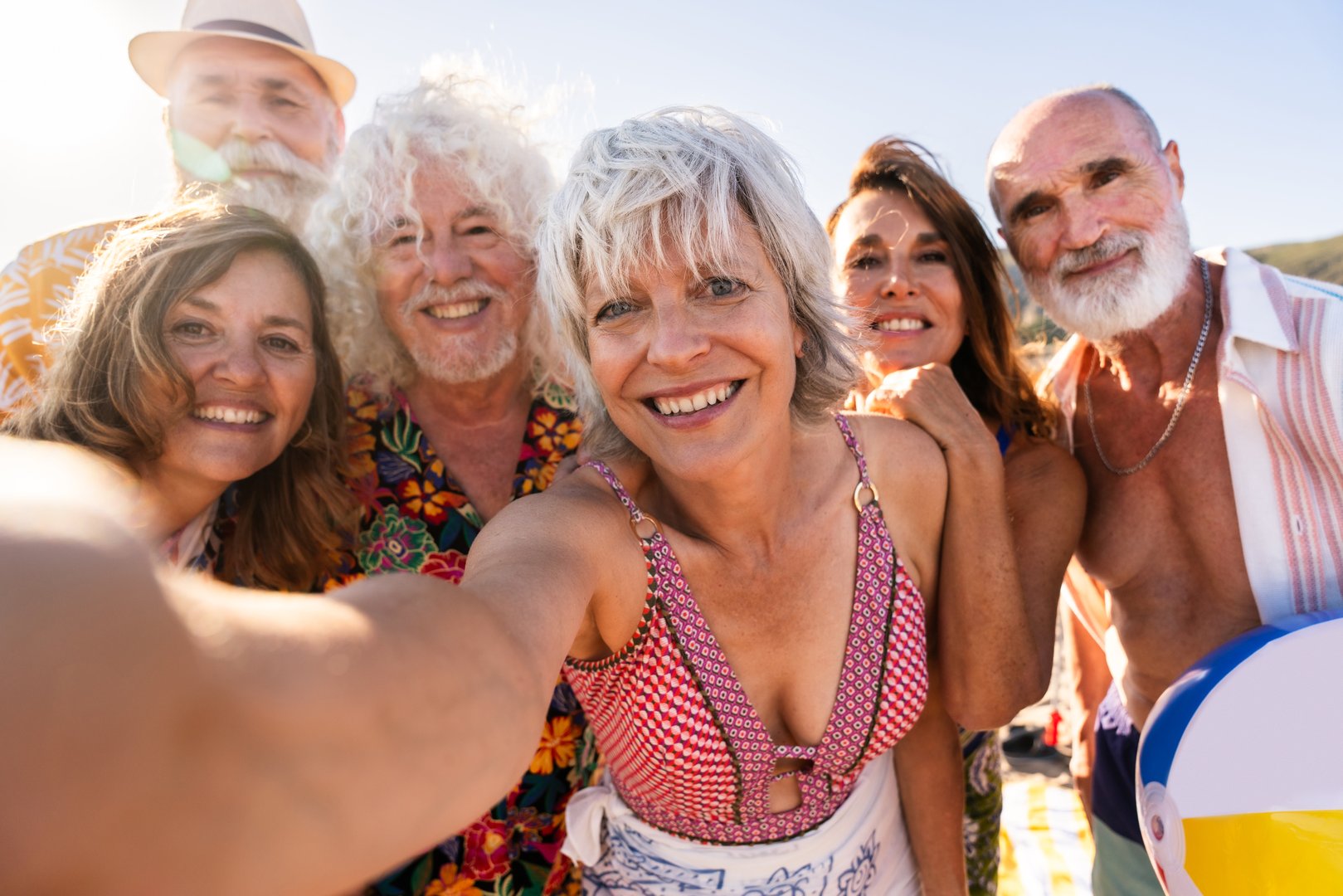 Happy group of senior friends bonding at the beach during summertime - Cheerful old and mature people having fun at the sea on summer vacation, elderly lifestyle concepts