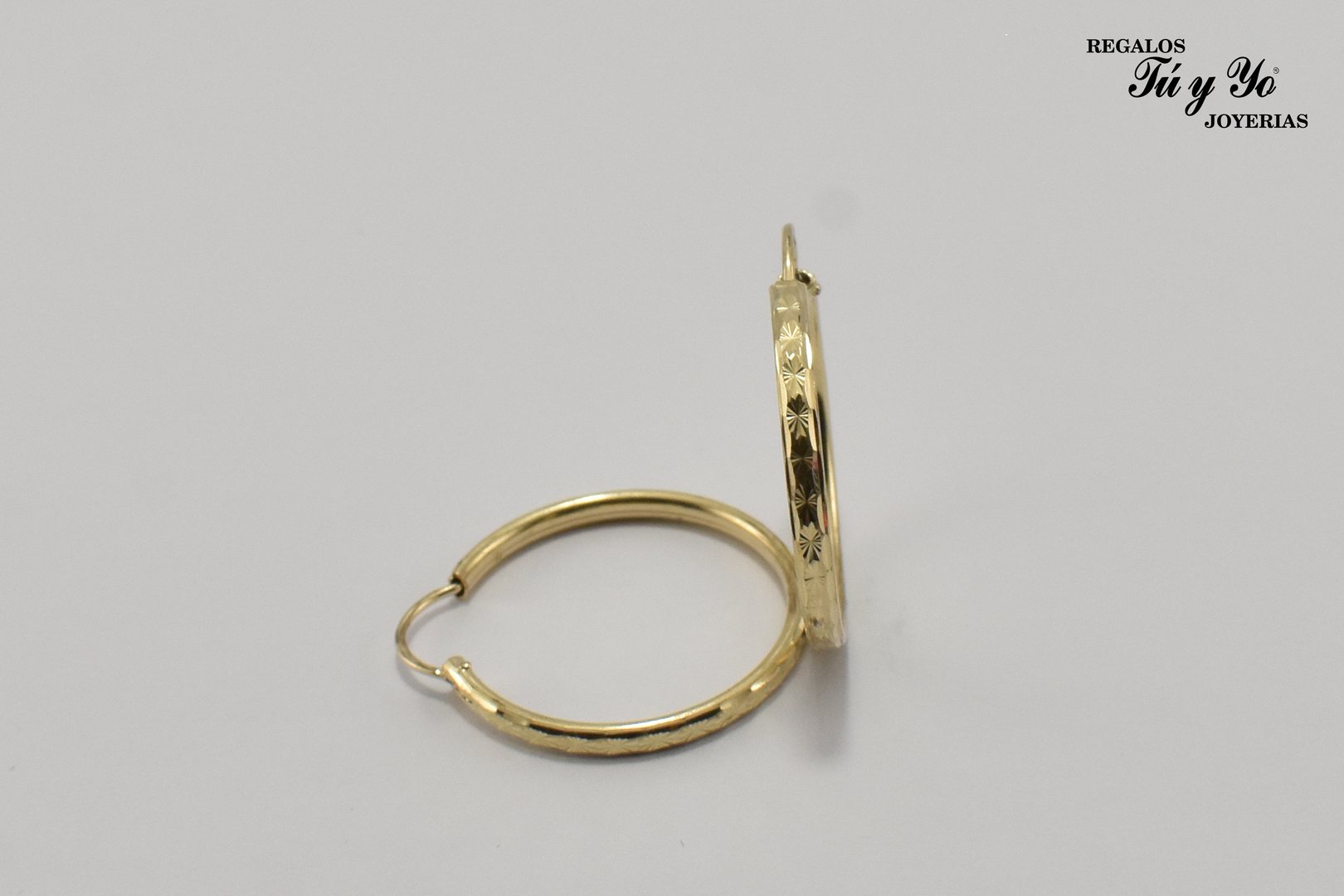 Gold hoop earring with floral engravings and a brand logo in the top right corner.