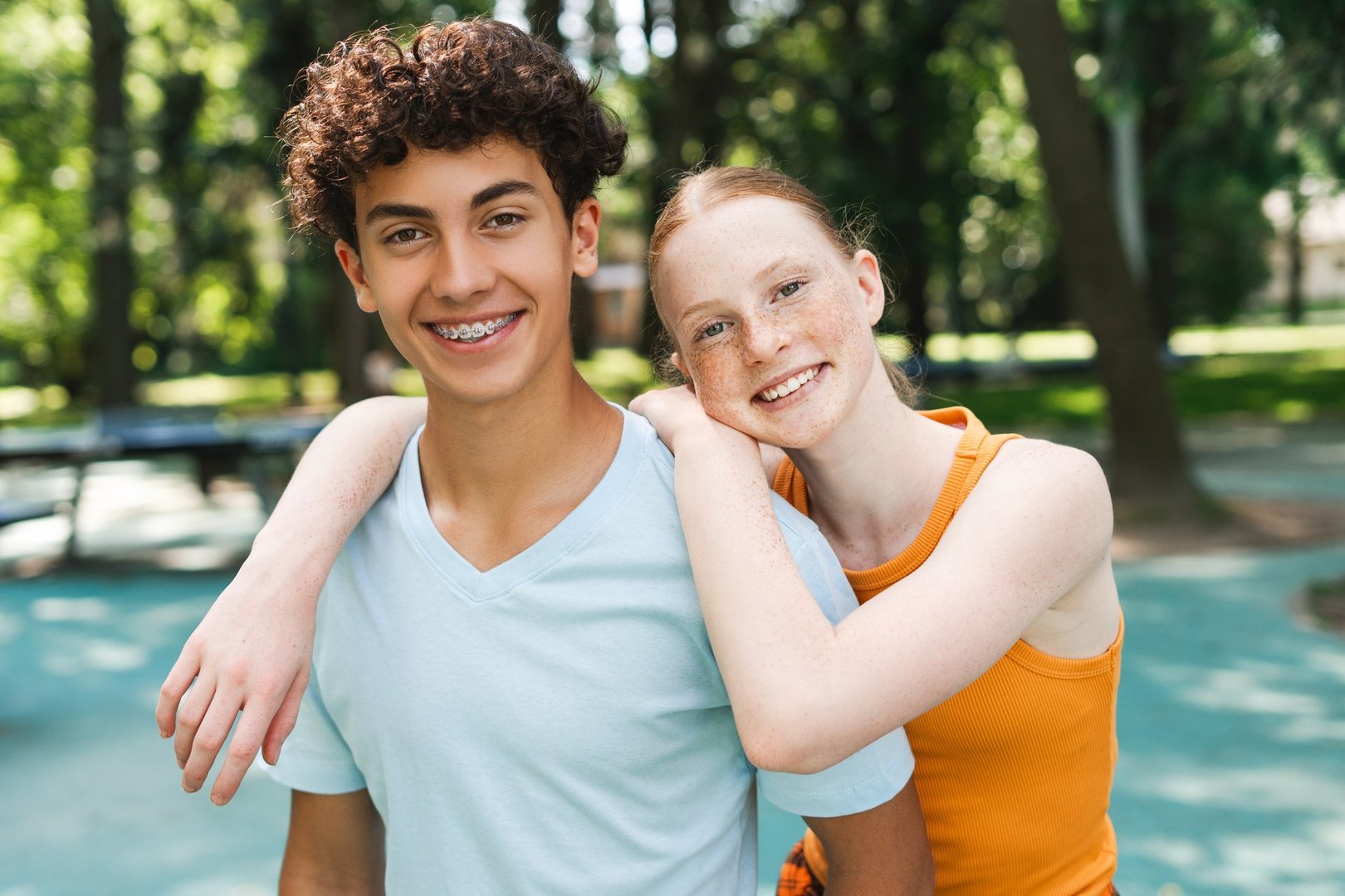 Portrait of happy red hair teenager girl hugging her male friend at the park. Children friendship concept